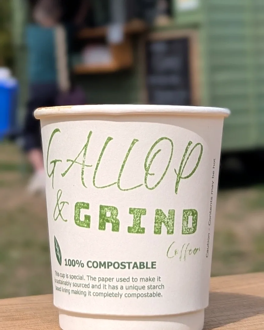 A Gallop & Grind compostable coffee cup on the counter, with the sage-green horsebox trailer in service behind
